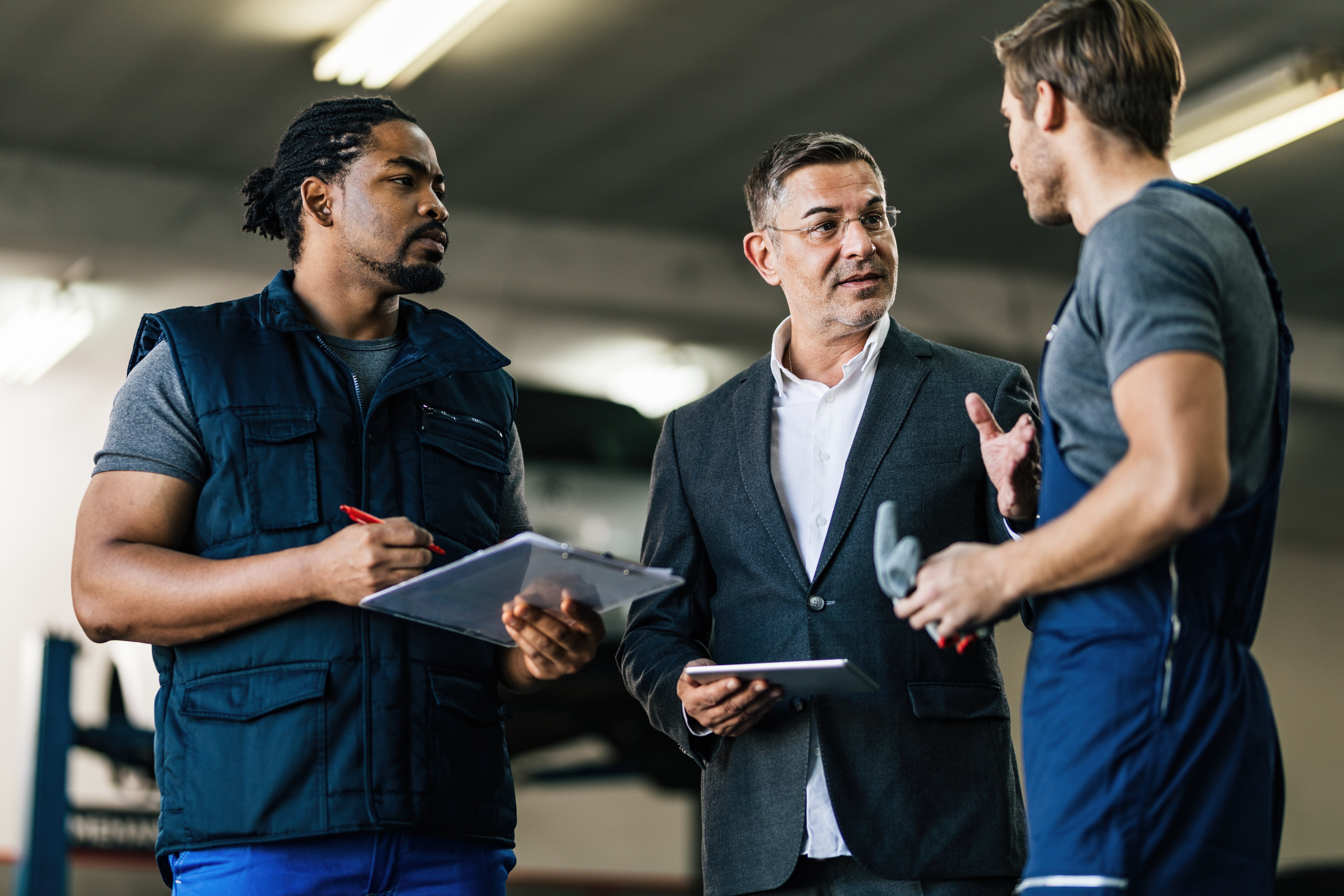 mid-adult-manager-using-digital-tablet-while-talking-car-mechanics-auto-repair-shop (1)