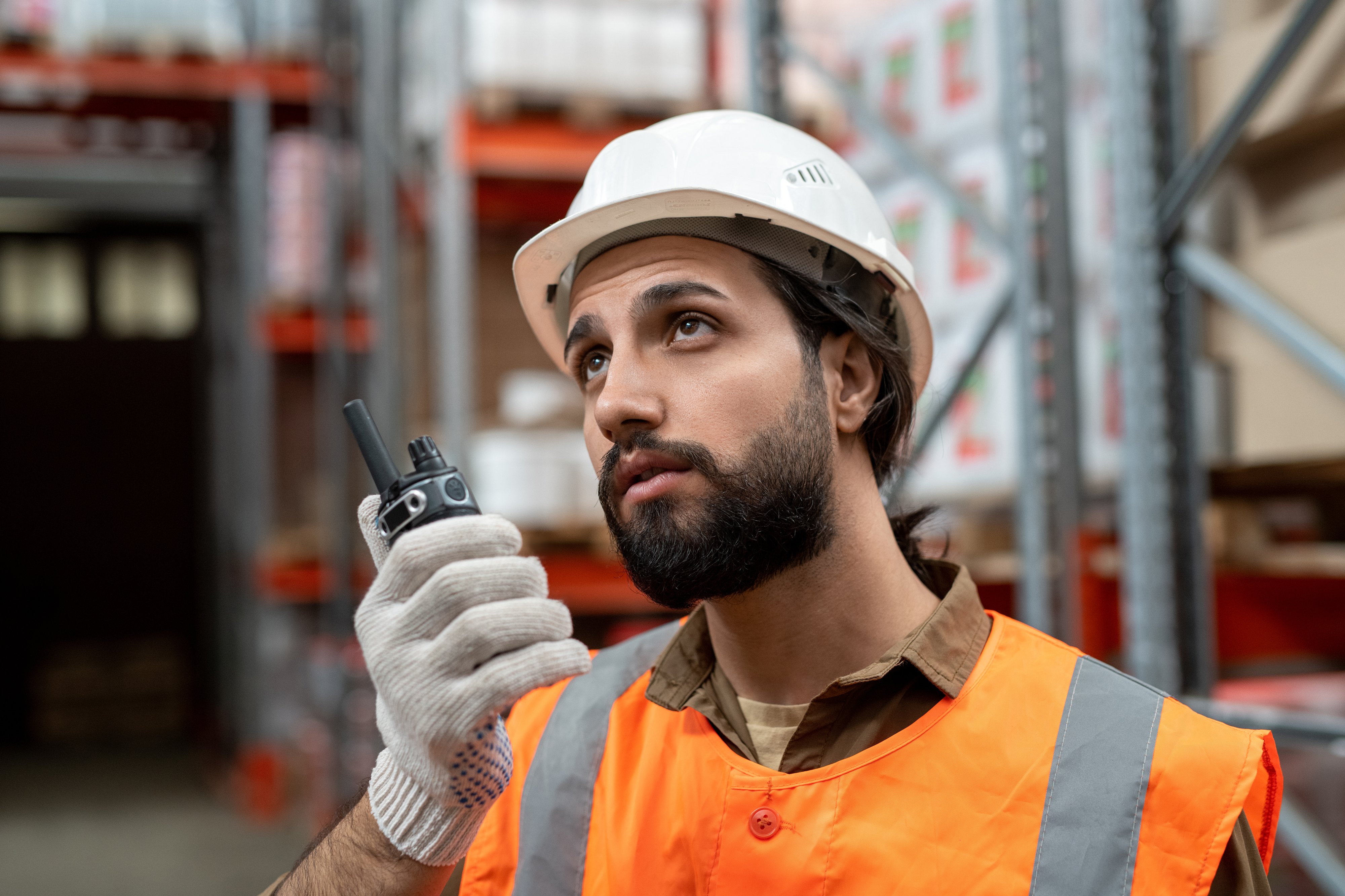 serious-mixed-race-warehouse-worker-white-hardhat-transmitting-message-colleague-via-walkie-talkie