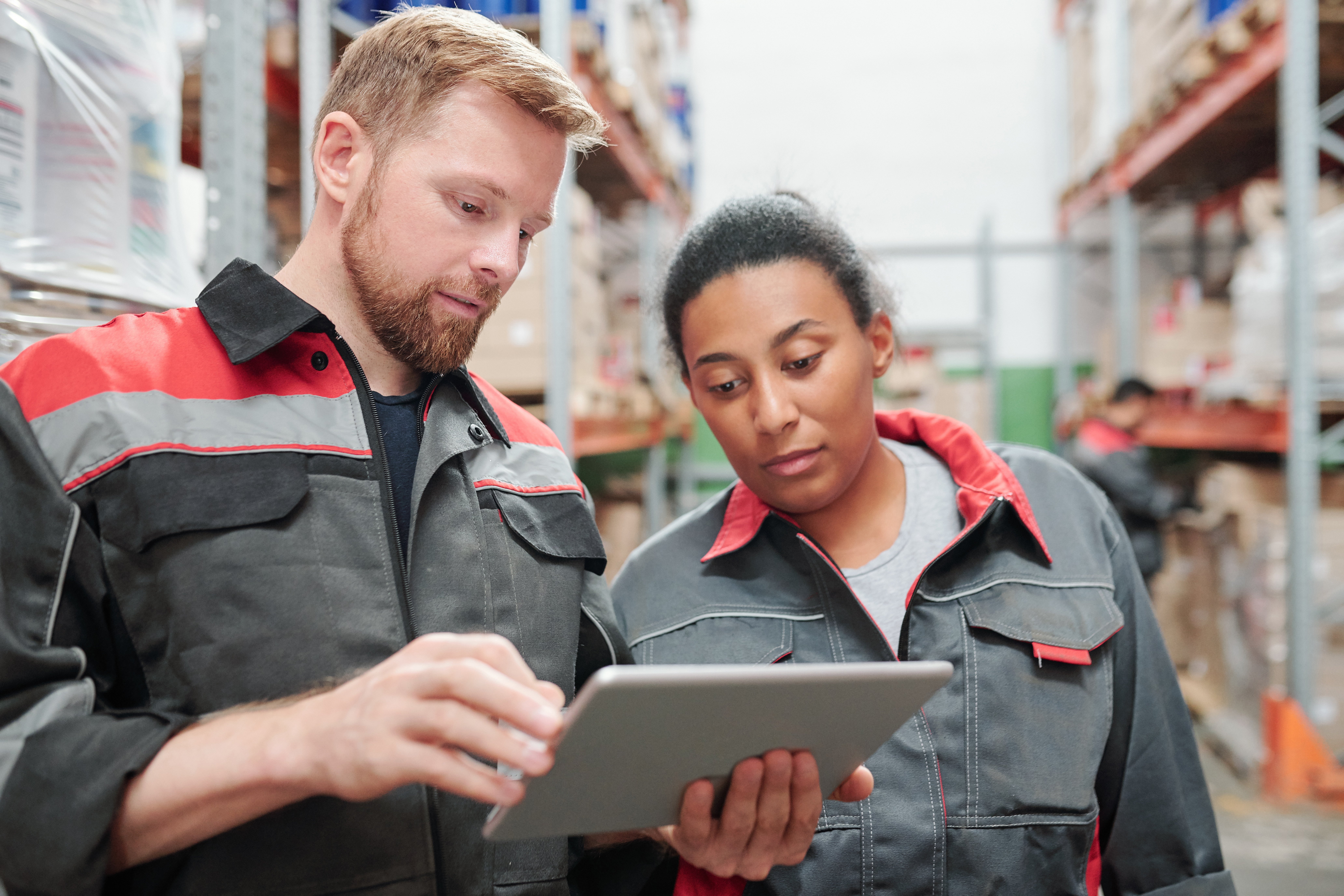 young-bearded-engineer-worker-warehouse-using-tablet-while-showing-his-mixed-race-female-colleague-list-new-goods